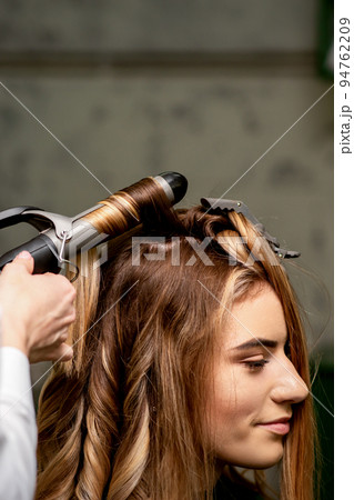 The female hairdresser is curling hair for a brown-haired young caucasian woman in a beauty salon 94762209