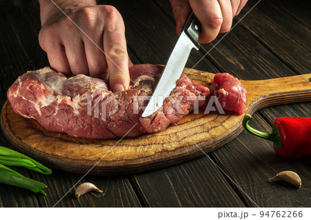 Butcher or chef cuts raw beef meat on a cutting board before baking. Hotel menu recipe idea Butcher or chef cuts raw beef meat on a cutting board before baking. Hotel menu recipe idea 94762266