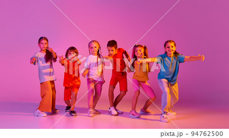 Dance group of happy, active little girls and boys in bright clothes in action isolated on pink background in neon. Concept of music, fashion, art, childhood Dance group of happy, active little girls and boys in bright clothes in action isolated on pink background in neon. Concept of music, fashion, art, childhood 94762500