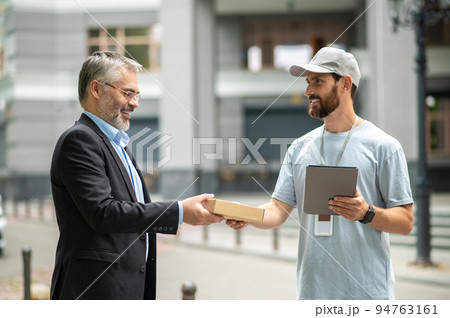 Bearded elegant businessman taking the box from a courrier Bearded elegant businessman taking the box from a courrier 94763161