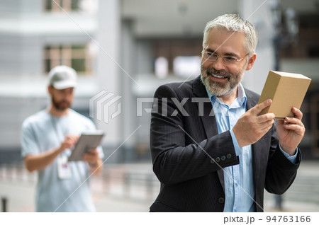 Bearded elegant businessman taking the box from a courrier Bearded elegant businessman taking the box from a courrier 94763166
