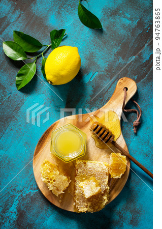 Natural Honey with Lemon. Honey in glass jar and dipper, Sweet Honeycombs on blue stone table. Top view flat lay background. Copy space. 94763865