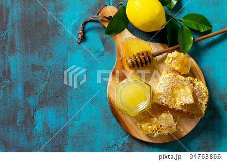 Natural Honey with Lemon. Honey in glass jar and dipper, Sweet Honeycombs on blue stone table. Top view flat lay background. Copy space. 94763866