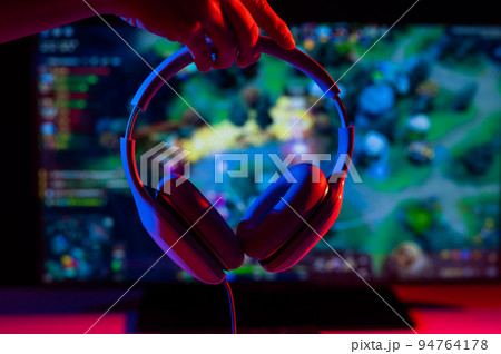 Woman holding headphones on the background of a computer game on the monitor. Woman holding headphones on the background of a computer game on the monitor. 94764178