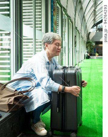 Portrait of senior adult elderly asian woman 60s smiling sitting with suitcase luggage bag and holding passport with ticket for travel concept. 94764293