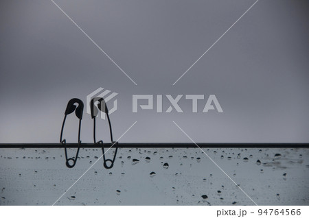 Safety pin couple sitting on glass wall with customizable space for text and ideas. Love and romance concept. Safety pin couple sitting on glass wall with customizable space for text and ideas. Love and romance concept. 94764566