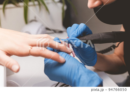 Manicurist cleans nails with a nail file drill before applying varnish. 94766050