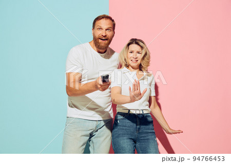 Studio shot of couple of young funny and happy man and woman having fun isolated over blue and pink background. 94766453