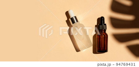 Frozen glass amber dropper bottle on beige background with tropical leave shadow. Banner. Pipette with serum, oil, retinol, hyaluronic acid. Healthcare beauty product. Eco-friendly anti-age cosmetics 94769431
