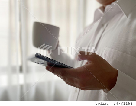 カップを持ってスマートフォンを操作する男性 カップを持ってスマートフォンを操作する男性 94771162