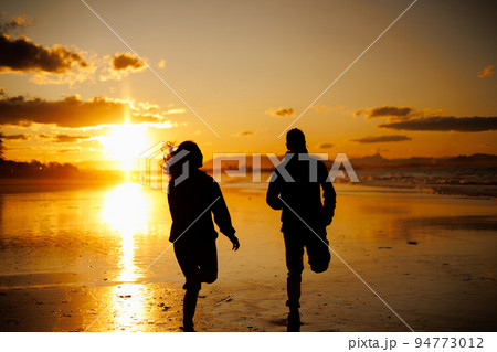 夕焼けの中で走る男女の後ろ姿シルエット 94773012