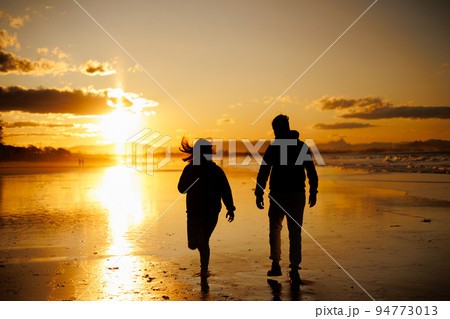 夕焼けの中男性を追いかける女性のシルエット 94773013