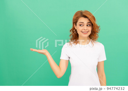 smiling redhead woman with curly hair presenting product looking aside, copy space, advertisement. smiling redhead woman with curly hair presenting product looking aside, copy space, advertisement. 94774232