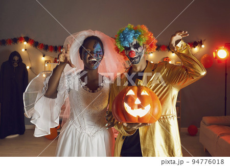 Two happy adult friends dressed in Halloween costumes of Dead Bride and Crazy Clown Two happy adult friends dressed in Halloween costumes of Dead Bride and Crazy Clown 94776018