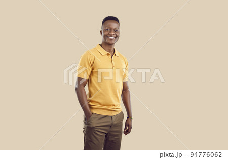 Young smiling African American man posing with one hand in pocket pants stands on beige background Young smiling African American man posing with one hand in pocket pants stands on beige background 94776062