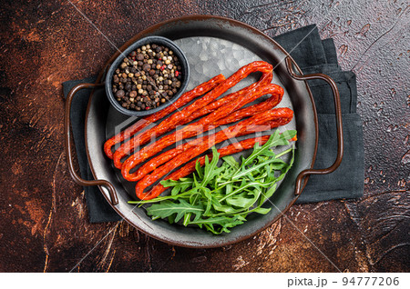 Dry smoked Kabanos or cabanossi traditional Polish thin sausages on a steel tray. Dark background. Top view 94777206