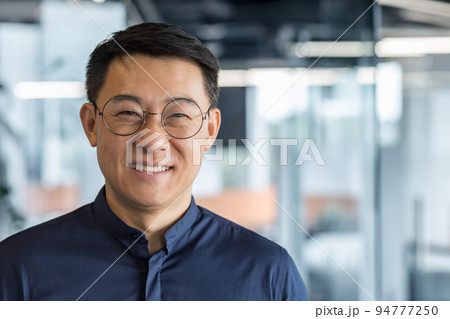 Close up photo portrait of successful young Asian investor, man in glasses smiling and looking at camera in shirt, businessman working inside modern office building, satisfied accountant financier. Close up photo portrait of successful young Asian investor, man in glasses smiling and looking at camera in shirt, businessman working inside modern office building, satisfied accountant financier. 94777250