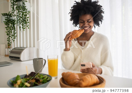 Portrait of young woman working from home eating croissant Portrait of young woman working from home eating croissant 94777398