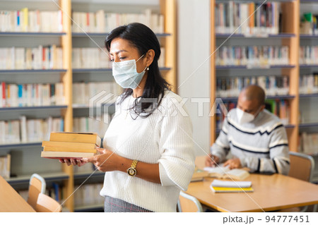 Adult latin american woman in protective mask visiting library 94777451