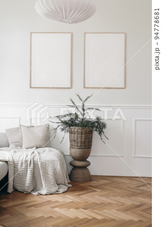 Christmas interior. Two blank vertical wooden picture frames mockups. White wall background.. Bed, sofa with linen cushions, blanket. Larch, pine tree branches in wicker basket, wooden coffee table. 94778681