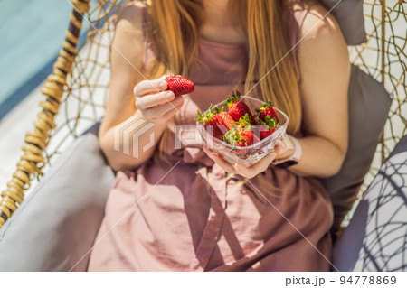 Portrait of gorgeous woman wearing beautiful dress sitting in a patio and eating strawberry 94778869