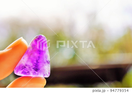 手に持って日の光に透かしたアメジストという名前の天然石 手に持って日の光に透かしたアメジストという名前の天然石 94779354
