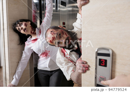 Couple of walkers leaving elevator to attack people in business office, walking dead horror apocalypse with devil possessed zombies . Eerie dramatic corpses brain eating monsters at workplace. 94779524