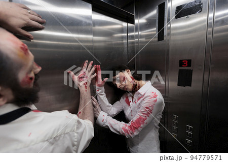 Creepy eerie zombies crawling on elevator walls, preparing terrifying sinister attack in company office. Brain eating walking dead killers looking aggressive and dangerous with bloody scars. 94779571