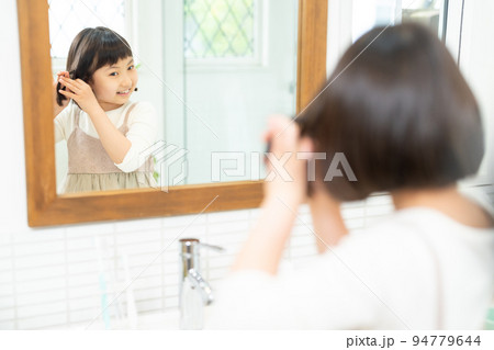鏡を見て髪の毛をセットする小学生の女の子 94779644