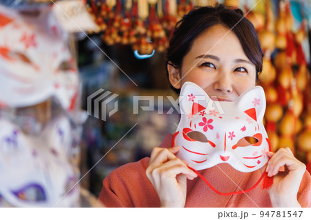 土産物店で狐のお面を持つ着物姿の女性 94781547