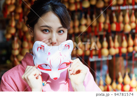 土産物店で狐のお面を持つ着物姿の女性 94781574