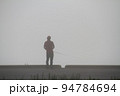 秋の早朝　朝霧の中で魚釣りをする男性 94784694