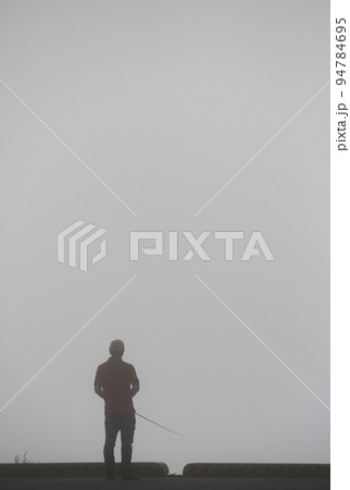 秋の早朝　朝霧の中で魚釣りをする男性 94784695