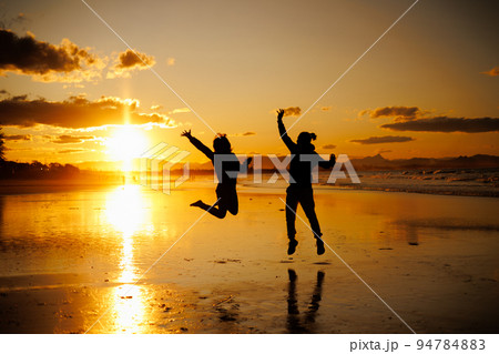 夕暮れ、ジャンプする男女のシルエット 94784883