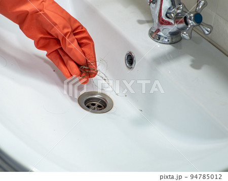 Hand in orange gloves holds many hair loss on filter in washbasin while cleaning Hand in orange gloves holds many hair loss on filter in washbasin while cleaning 94785012