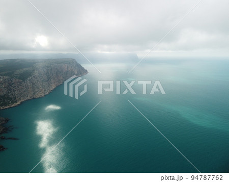 Aerial view from above on calm azure sea and volcanic rocky shores. Small waves on water surface in motion blur. Nature summer ocean sea beach background. Nobody. Holiday, vacation and travel concept 94787762