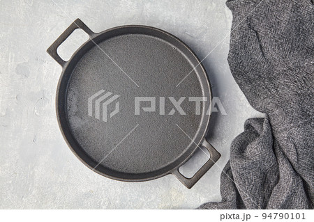Black cast iron empty frying pan and gray kitchen towel on a gray concrete background Black cast iron empty frying pan and gray kitchen towel on a gray concrete background 94790101