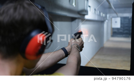 Shooter man holding gun in hand and shooting at a target rear view Shooter man holding gun in hand and shooting at a target rear view 94790176