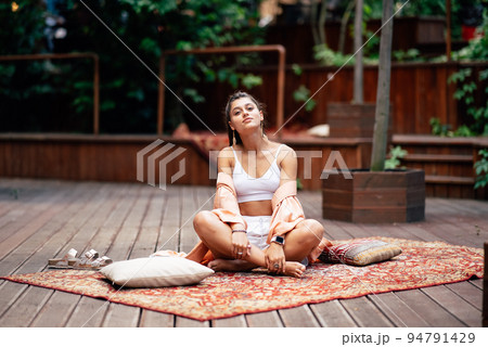 Young woman is practising yoga sitting on a wooden podium 94791429