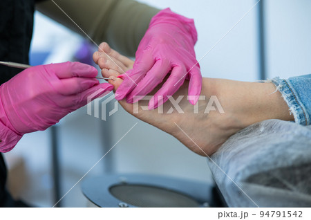 Podiatrist makes a pedicure to a client. The master conducts hygiene of the toes with a metal stick. Podiatrist makes a pedicure to a client. The master conducts hygiene of the toes with a metal stick. 94791542