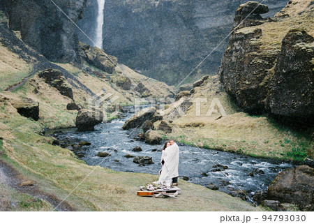 Man and woman in a blanket stand on the banks of a river in the mountains. Iceland 94793030
