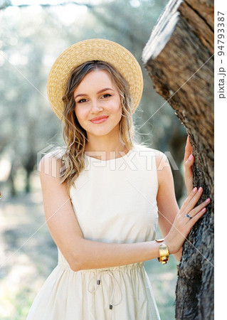 Girl in a straw hat stands near a tree in an olive grove. Portrait 94793387