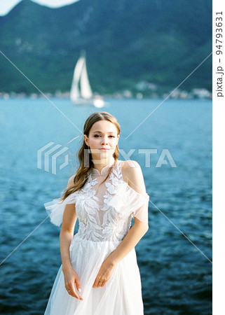 Bride stands against the backdrop of the blue sea and a passing sailboat Bride stands against the backdrop of the blue sea and a passing sailboat 94793631
