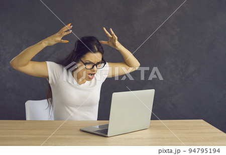 Angry and frustrated woman feels stressed and screams furiously while sitting in front of a laptop. 94795194
