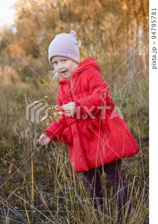 A little girl in a red coat walks in nature in an autumn grove. The season is autumn 94795781