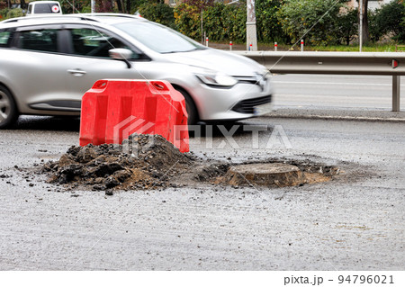 A red road shield blocks a sewer manhole from a speeding car in blur. 94796021