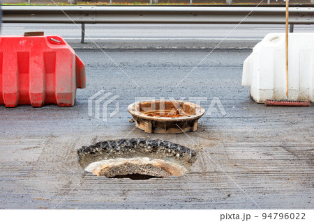 Red and white road shields protect an open sewer manhole during its repair on the carriageway. Red and white road shields protect an open sewer manhole during its repair on the carriageway. 94796022