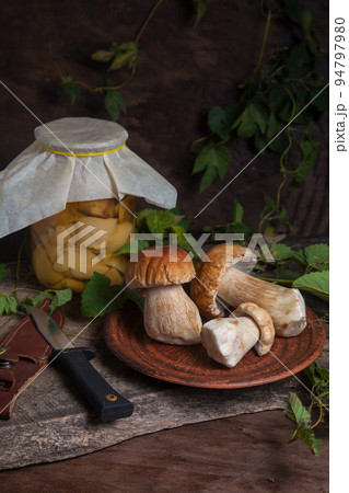 Clay plate with porcini mushroom commonly known as Boletus Edulis, glass jar with canned mushrooms and knife on vintage wooden background.. Clay plate with porcini mushroom commonly known as Boletus Edulis, glass jar with canned mushrooms and knife on vintage wooden background.. 94797980