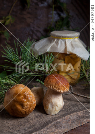 Two porcini mushrooms commonly known as Boletus Edulis and glass jar with canned mushrooms on vintage wooden background.. Two porcini mushrooms commonly known as Boletus Edulis and glass jar with canned mushrooms on vintage wooden background.. 94797981