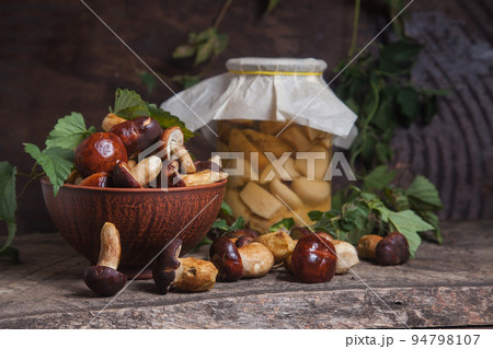 Pile of Imleria Badia or Boletus badius mushrooms commonly known as the bay bolete with canned mushroom in glass jar on vintage wooden background.. Pile of Imleria Badia or Boletus badius mushrooms commonly known as the bay bolete with canned mushroom in glass jar on vintage wooden background.. 94798107